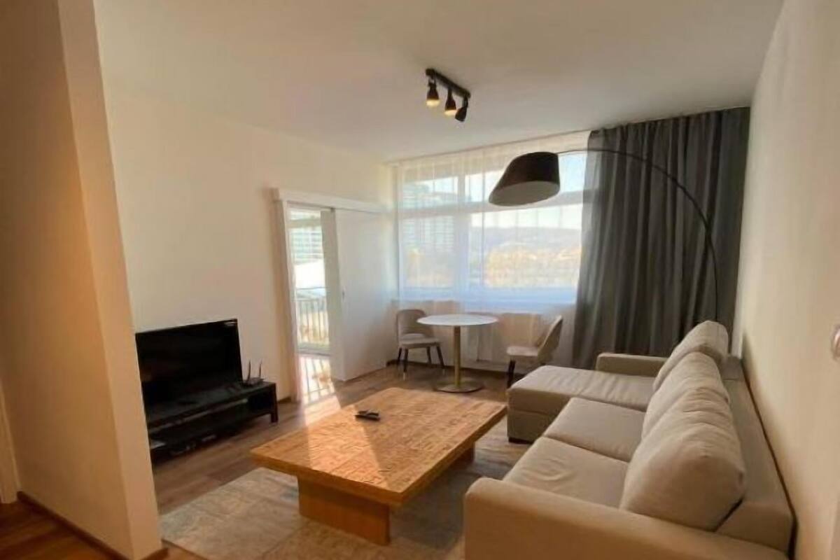 Un salon moderne avec une table basse en bois, un canapé beige et un téléviseur.
