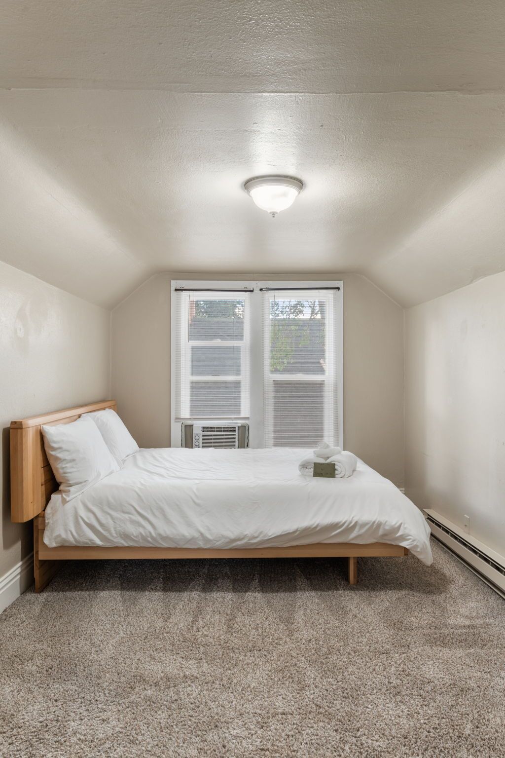 Ein Schlafzimmer mit Bett, Deckenleuchte, Heizkörper und Fenster mit Jalousien.