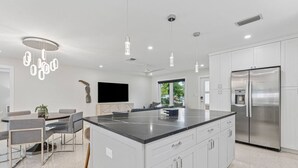 Una cocina moderna con una isla central, armarios blancos, electrodomésticos de acero inoxidable e iluminación colgante.