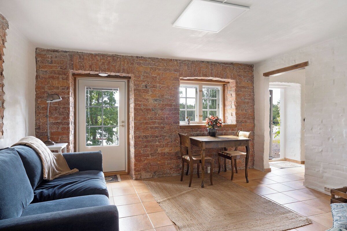 Una habitación con pared de ladrillo, una mesa de comedor con sillas, un sofá y una ventana.