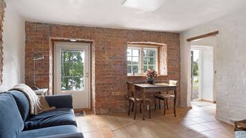 A room with a brick wall, a dining table with chairs, a sofa, and a window.