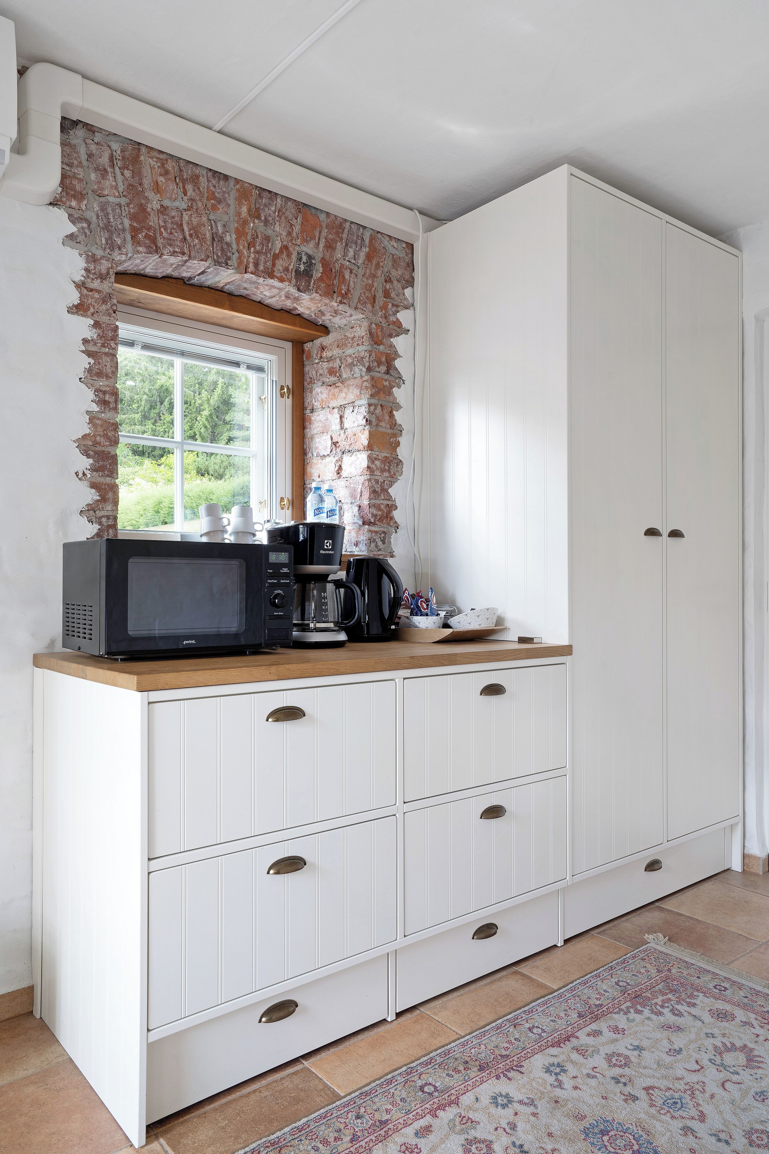 A kitchen with a brick wall, a window, and a white cabinet with drawers.