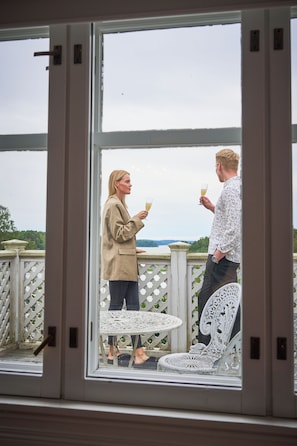 Two people standing by a window, holding drinks, with a view of a white fence and outdoor furniture. - Villa Wolax (Kaarina)