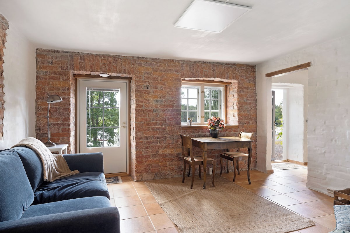 A room with a brick wall, a dining table with chairs, a sofa, and a window.