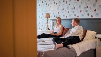 A bedroom with a bed, a nightstand, a lamp, and a floral wallpaper.