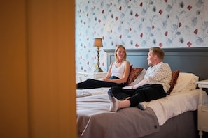 A bedroom with a bed, a nightstand, a lamp, and a floral wallpaper. - Villa Wolax (Kaarina)