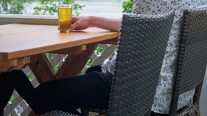 Una persona sentada a una mesa de madera con un vaso de jugo de naranja, con vista a un lago y árboles al fondo.