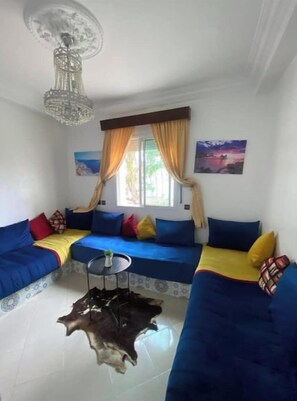A living room with a blue sofa set, a chandelier, a small round table, and a large window with curtains. - Entire apartment (Tanger)