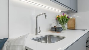 A modern kitchen with a stainless steel sink, a faucet, and a countertop. There are two jars with the text 'ONESTAY' on them, a vase with tulips, and a wooden cutting board.