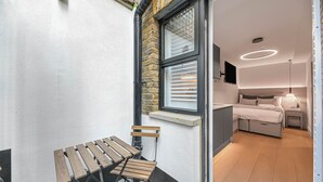 A modern room with a bed, bedside table, and a window with blinds.