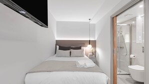 A modern hotel room with a bed, bedside table, lamp, and a glass-enclosed shower area.