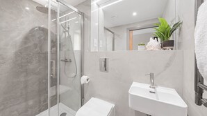 A modern bathroom with a glass-enclosed shower, a white sink, and a toilet.