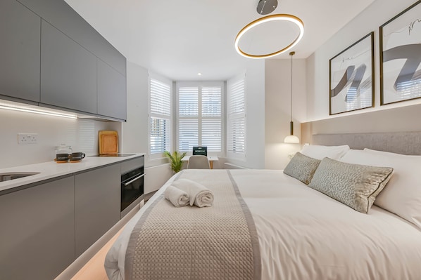 A modern hotel room with a bed, a desk, and a kitchenette.