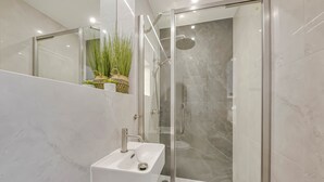 Ein modernes Badezimmer mit einer gläsernen Duschkabine, einem weißen Waschbecken und einer Topfpflanze.