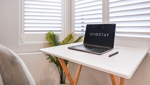 Ein Laptop auf einem weißen Tisch, daneben ein Stift, vor einem Fenster mit Jalousien.