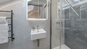 Moderni kylpyhuone, jossa on lasinen suihkuseinä, valkoinen pesuallas ja pyyhekoukku.