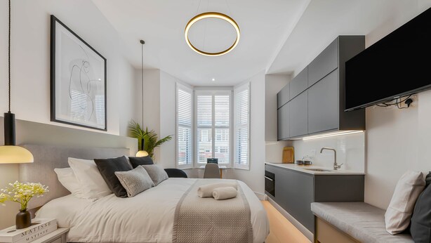 A modern bedroom with a bed, bedside table, lamp, artwork, and a TV mounted on the wall.
