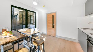 A modern kitchen with a wooden table and bar stools, a large window, and a door leading to another room.