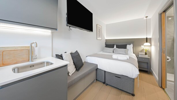 A modern hotel room with a bed, bedside table, TV, and a built-in sink. - Studio 12 @ OneStay Maida Vale (London)