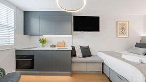 A modern room with a kitchenette, a flat-screen TV, a bed with pillows, and a framed artwork on the wall. - Studio 12 @ OneStay Maida Vale (London)