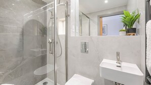 A modern bathroom with a glass-enclosed shower, a white sink, and a mirror. - Studio 12 @ OneStay Maida Vale (London)