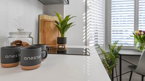 A modern kitchen with a white countertop, a glass jar with cookies, and two black mugs with 'oneSTAY' text.
