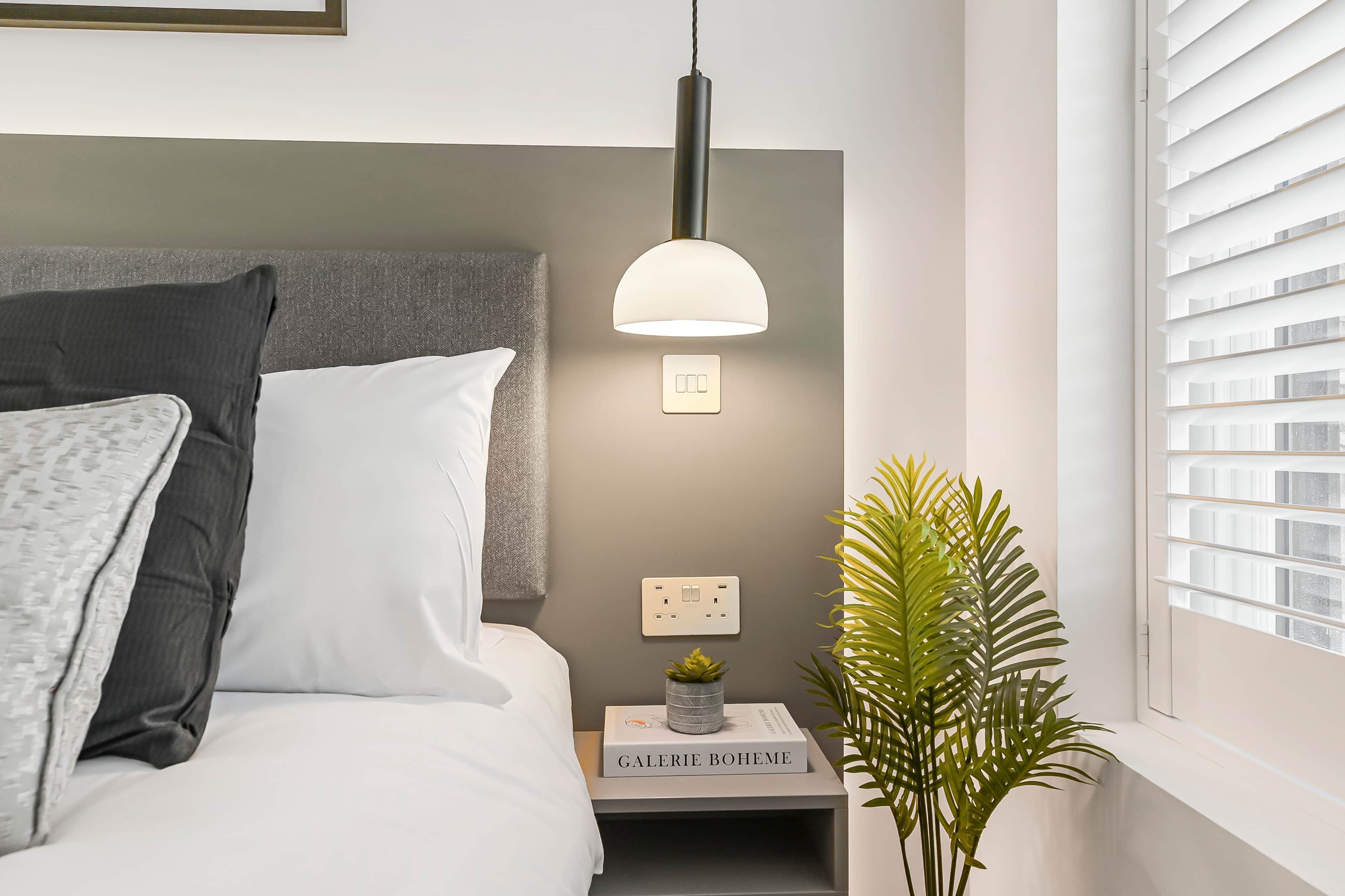Ein ordentlich eingerichtetes Schlafzimmer mit Bett, Nachttisch, Lampe und einem Fenster mit Jalousien.
