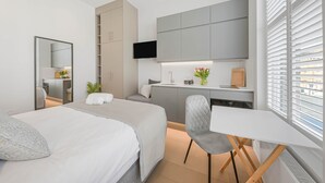 A modern hotel room with a bed, a desk, a TV, and a window with blinds.