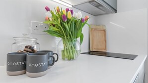 A kitchen counter with a vase of tulips, a jar of nuts, and two mugs with 'oneSTAY' branding.