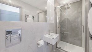 A modern bathroom with a glass-enclosed shower, a sink, and a toilet paper holder.