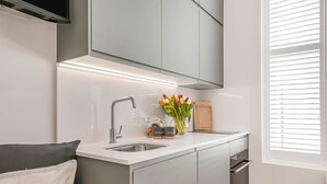 A modern kitchen with a built-in oven, a sink, and a window with blinds.