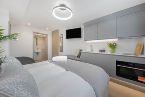 A modern hotel room with a bed, a desk, a television, and a kitchen area.