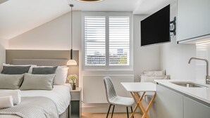 Un dormitorio moderno con cama, mesita de noche, lámpara y vistas a la ciudad a través de amplios ventanales.