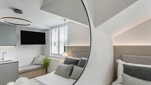 Una habitación de hotel moderna con cama, mesita de noche, espejo, televisor y ventana.