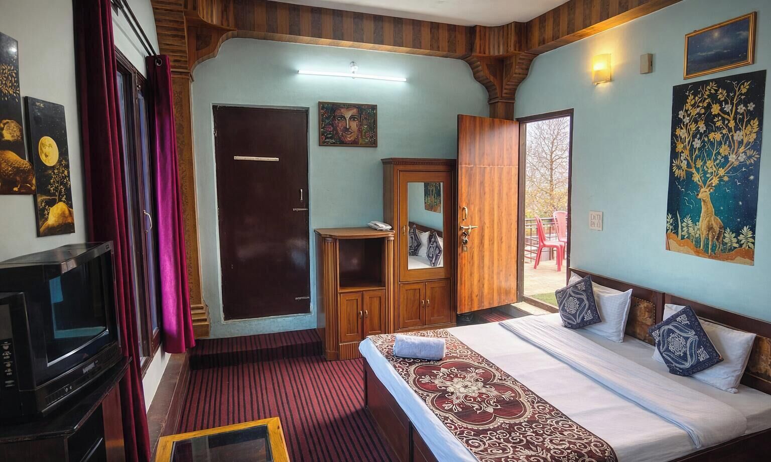 Habitación de hotel con cama, televisor, armario y puerta que da a un área exterior.