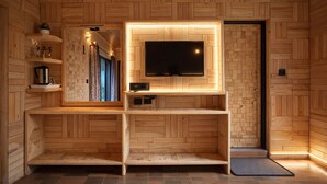 Een houten interieur met een aan de muur bevestigde televisie, een klein plankje met een waterkoker en een raam met gordijnen.