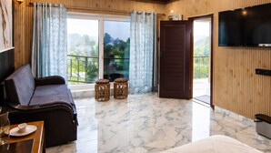 Een moderne hotelkamer met een houten plafond, een groot bed, een bank, een televisie en een balkon met uitzicht op groen.