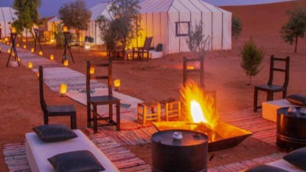 A desert camp with tents, lounge chairs, and a central fire pit. - Les Pyramides Merzouga Camp (Merzouga)