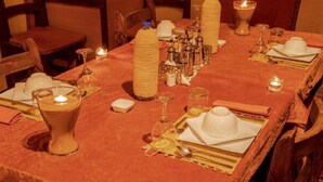 A dining table set with a red tablecloth, candles, and various glassware and dishes. - Les Pyramides Merzouga Camp (Merzouga)