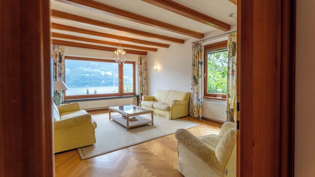 A spacious living room with wooden beams, a large window with a view, and a chandelier. - Chalet Birkmayer by we rent (Zell am See)