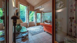 A room with a wooden ceiling, a large window with curtains, a pink armchair, a green vase, and a chandelier. - Chalet Birkmayer by we rent (Zell am See)