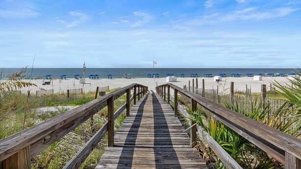 A wooden boardwalk leading to a beach with umbrellas and lounge chairs.