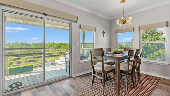 Comedor con una mesa dispuesta para seis personas, ventanas amplias con persianas y vistas a una zona boscosa.