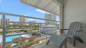 A balcony with a view of a swimming pool, a chair, and a cityscape with tall buildings.
