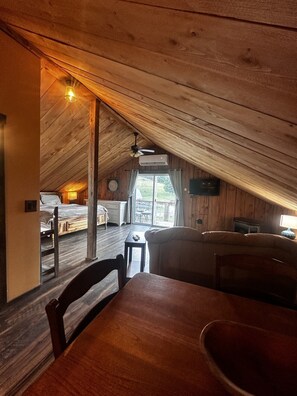 Acogedor cuarto ático con techo de madera, una mesa de comedor y vista al patio trasero por una ventana.