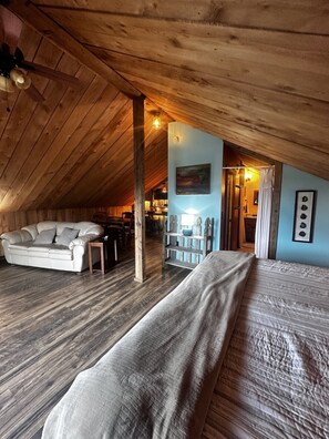 An attic bedroom with a sloped ceiling, a sofa, a bed, and a dining area.