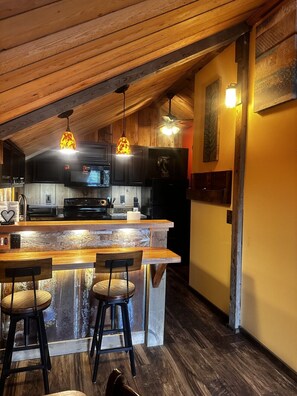 A kitchen with wooden ceiling beams, a bar area with stools, and pendant lighting.