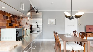 A modern kitchen with a built-in oven, a coffee machine, and a toaster. There is a dining area with a wooden table and chairs. - GuestReady - Charming Covent Garden Retreat (London)