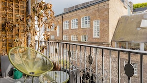A balcony with a green chair and a glass table, overlooking a brick building with multiple windows. - GuestReady - Charming Covent Garden Retreat (London)