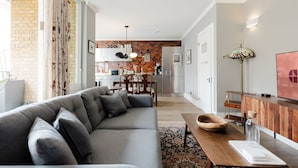 A modern living room with a grey sofa, wooden dining table, and a kitchen in the background. - GuestReady - Charming Covent Garden Retreat (London)